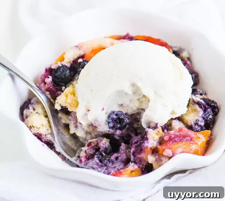 Perfect Blueberry Peach Cobbler Recipe for Summer Desserts 5 fork digging into a bowl of cobbler with vanilla ice cream on top