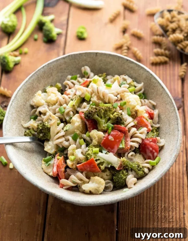 ceramic bowl of pasta salad with roasted veg on a wooden table