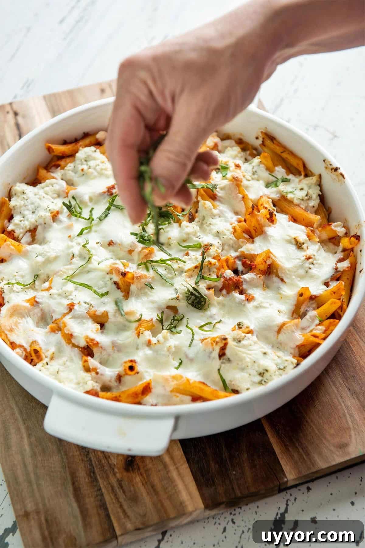 Top Baked Pasta Recipes for Comforting Weeknight Dinners 3 Woman sprinkling thinly-sliced basil onto a dish of Baked Pasta with Bolognese Sauce.