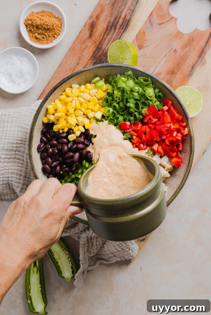 Southwest dressing being poured over top of southwest chicken salad ingredients in a large bowl.