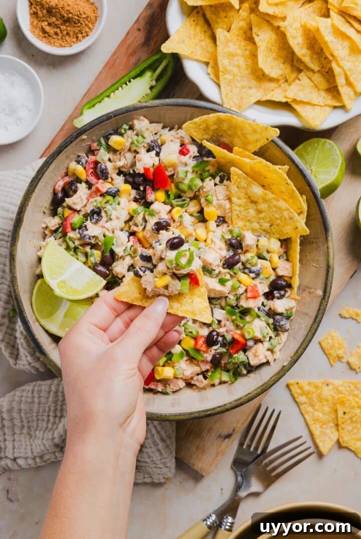 Southwest chicken salad being scooped with a tortilla chip with a woman's hand.