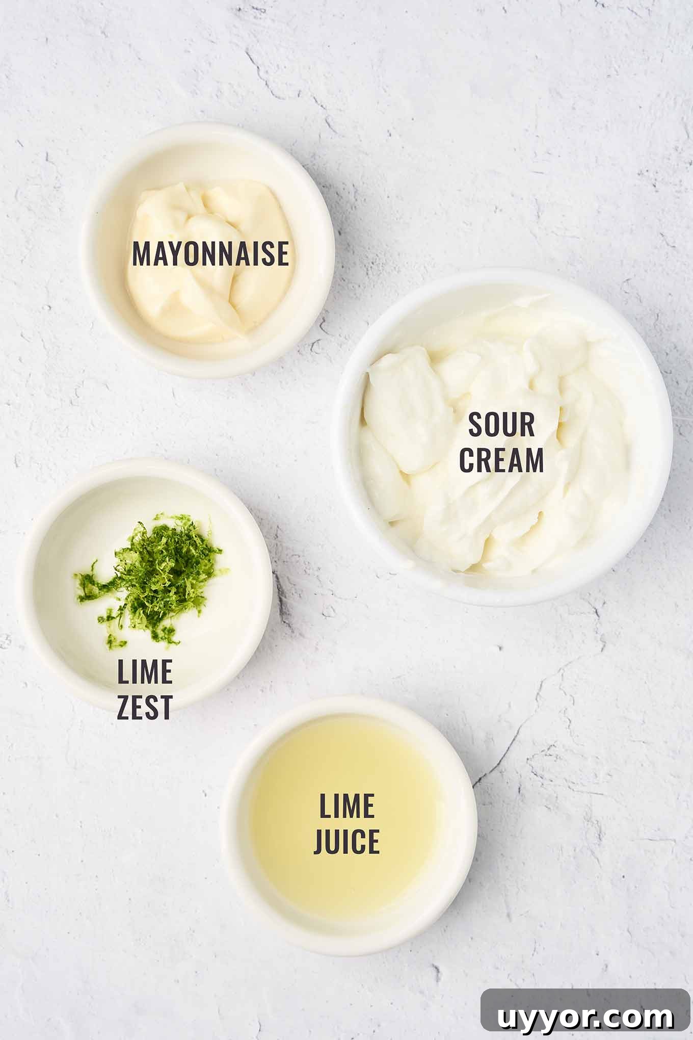 Spicy Shrimp Tacos with Caramelized Sweet Plantains 4 A labeled, overhead view of the ingredients for lime crema topping for shrimp tacos, including mayonnaise, sour cream, lime zest, and lime juice - all in small white bowls.