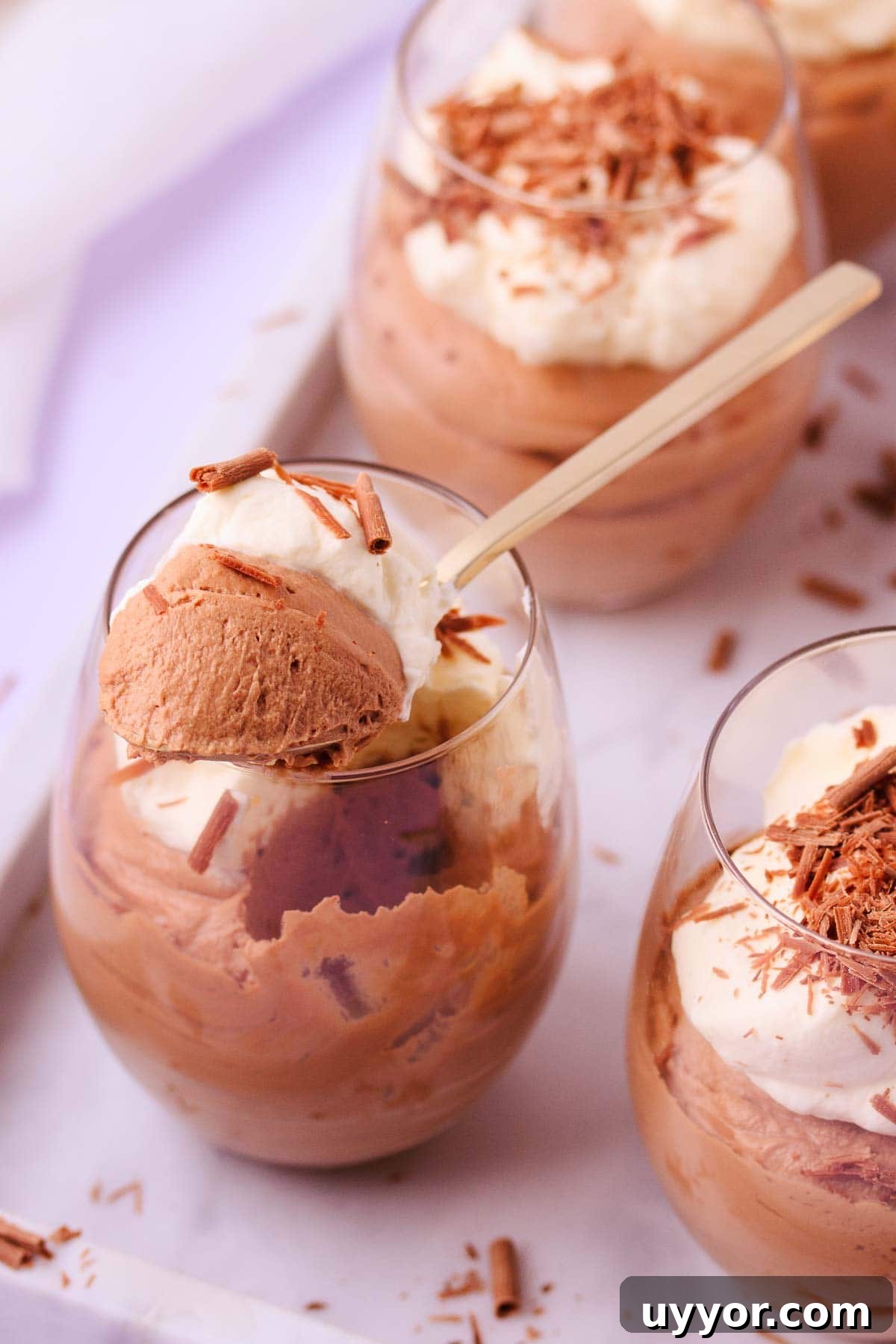 Close up of a spoonful of milk chocolate mousse resting on the rim of the glass, showing the fluffy mousse texture. 