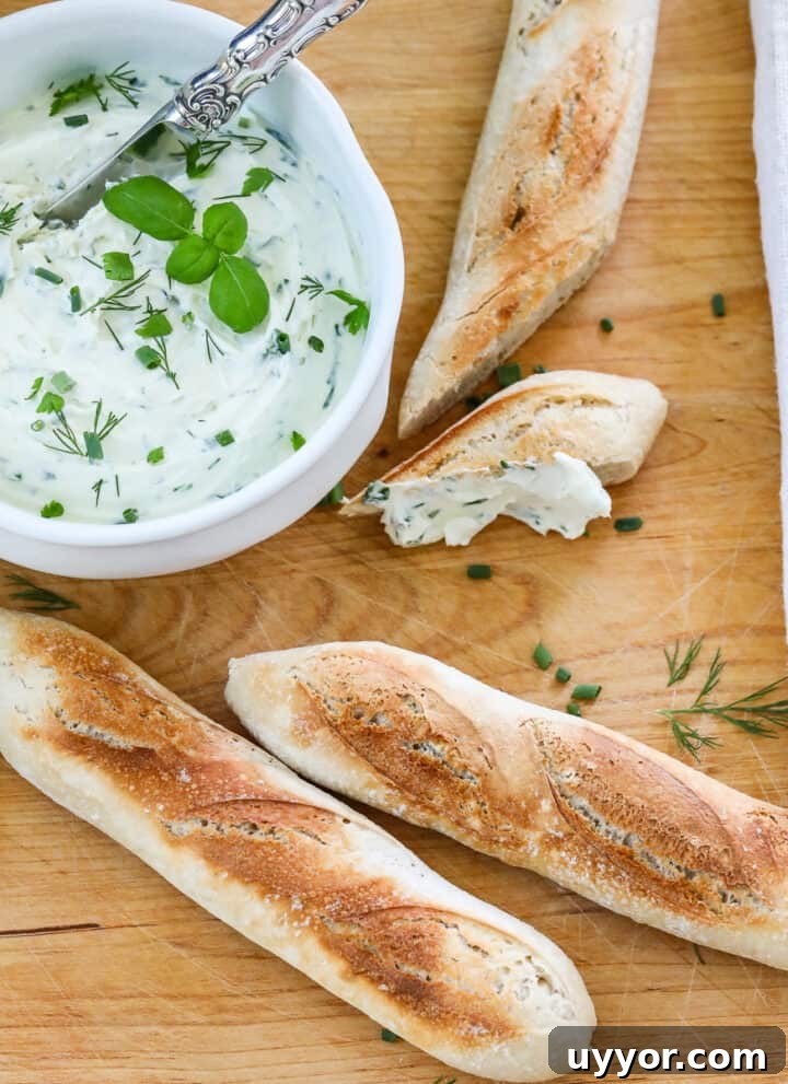A wooden cutting board with small baguettes sliced open with a white bowl of whipped creamed cheese spread on a slice.