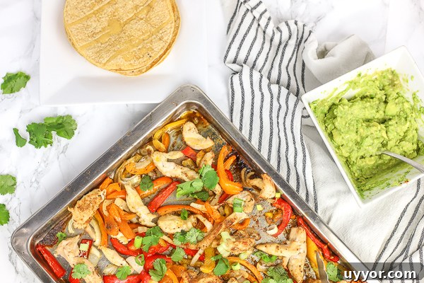 sheet pan chicken fajitas on a baking sheet with corn tortillas and guacamole on the side