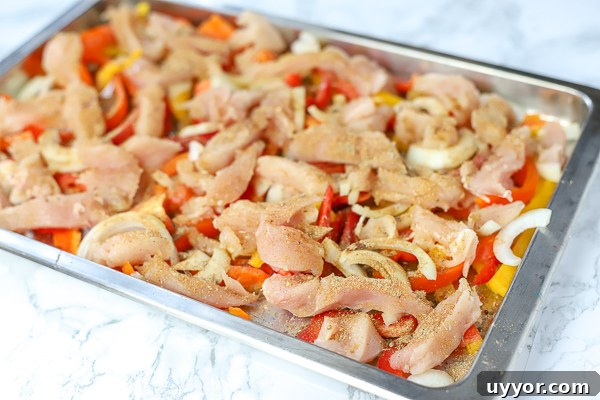 raw chicken, peppers, onions, and seasonings on a sheet pan to make sheet pan chicken fajitas