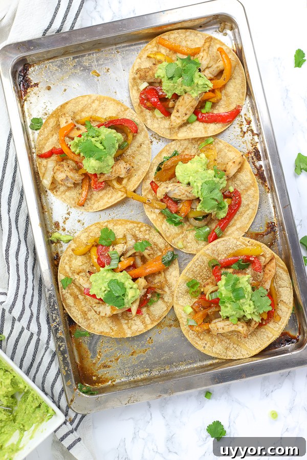 sheet pan chicken fajitas on tortillas and topped with guacamole