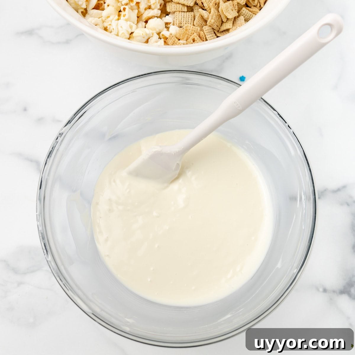 Patriotic Red White & Blue Chex Mix Recipe for 4th of July 4 Melted almond bark in a clear bowl with a white spatula. Cereal and popcorn in a bowl in the background.