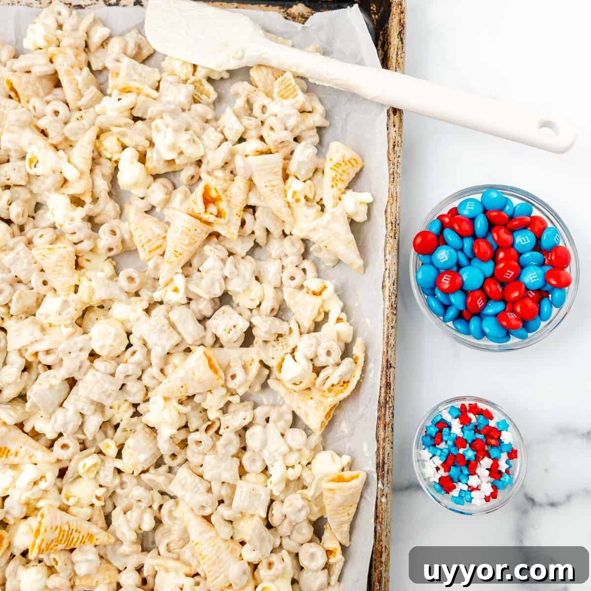 Patriotic Red White & Blue Chex Mix Recipe for 4th of July 7 Cereal, corn chips, and popcorn, coated in melted almond bark on a sheet pan. Red and blue M&Ms and sprinkles on a side