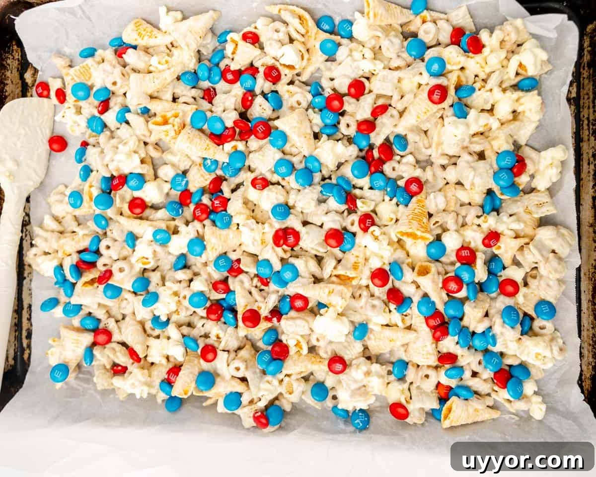Patriotic Red White & Blue Chex Mix Recipe for 4th of July 8 A baking sheet lined with parchment paper holds a mixture of popcorn, cereal pieces, and red and blue candy-coated chocolates.