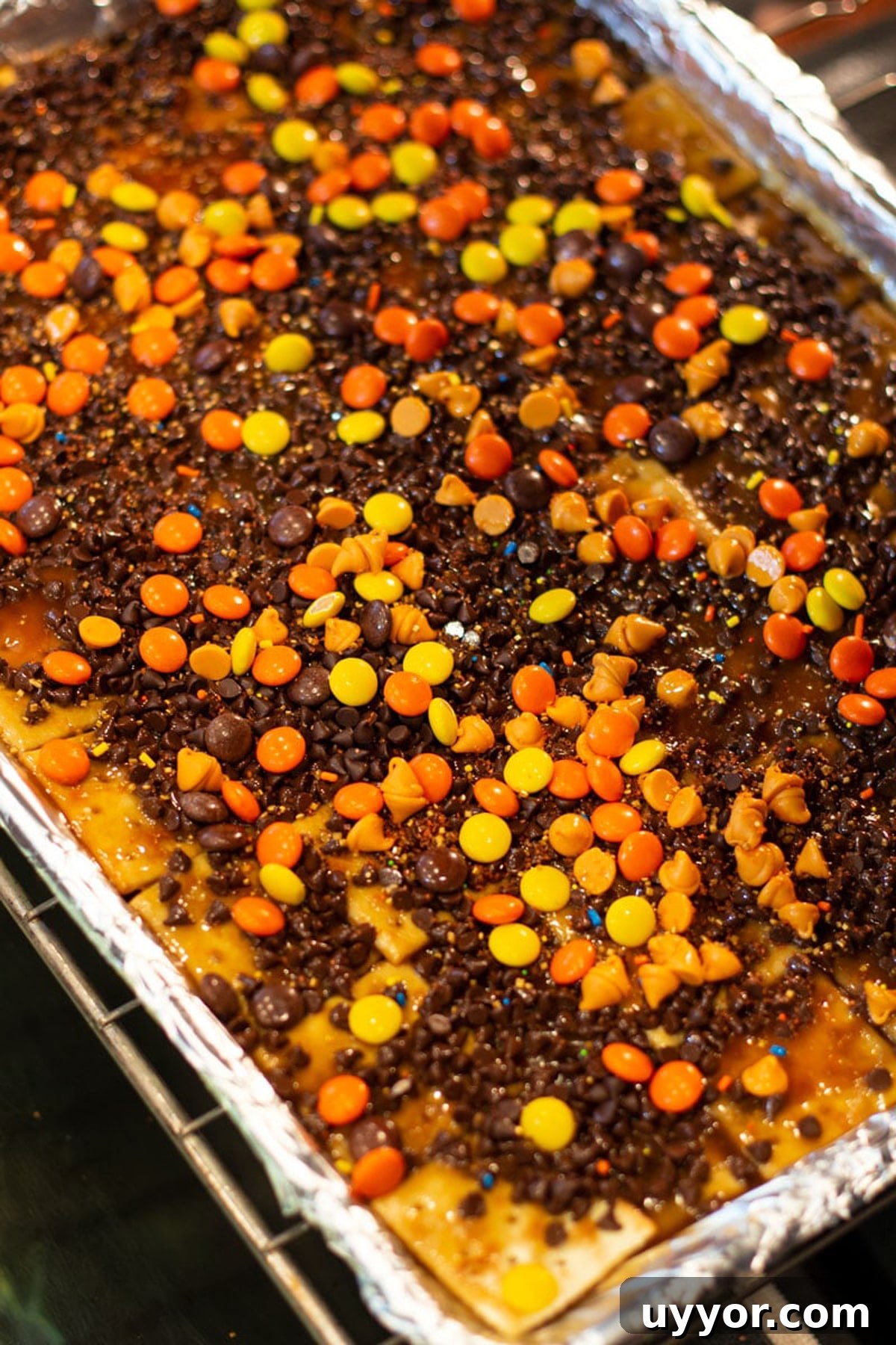 Halloween Crack Candy Recipe: Sweet & Crunchy Toffee Treat 12 Cookie Sheet with chocolate chip morsels, Reese's Pieces, caramel, crackers and pecans being placed in the oven.