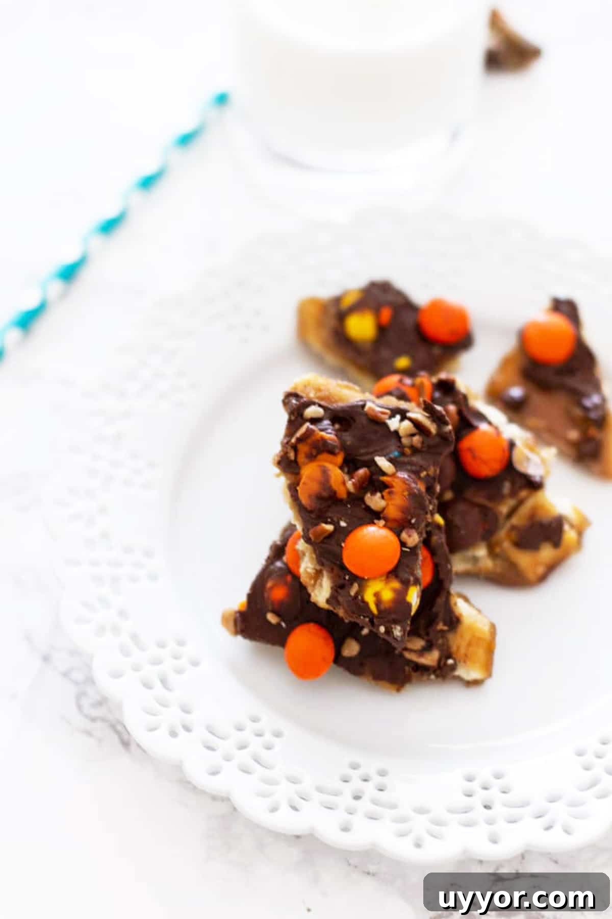 Halloween Crack Candy Recipe: Sweet & Crunchy Toffee Treat 14 White plate with pieces of Halloween Candy Bark topped with reese's pieces, milk and straw on table.
