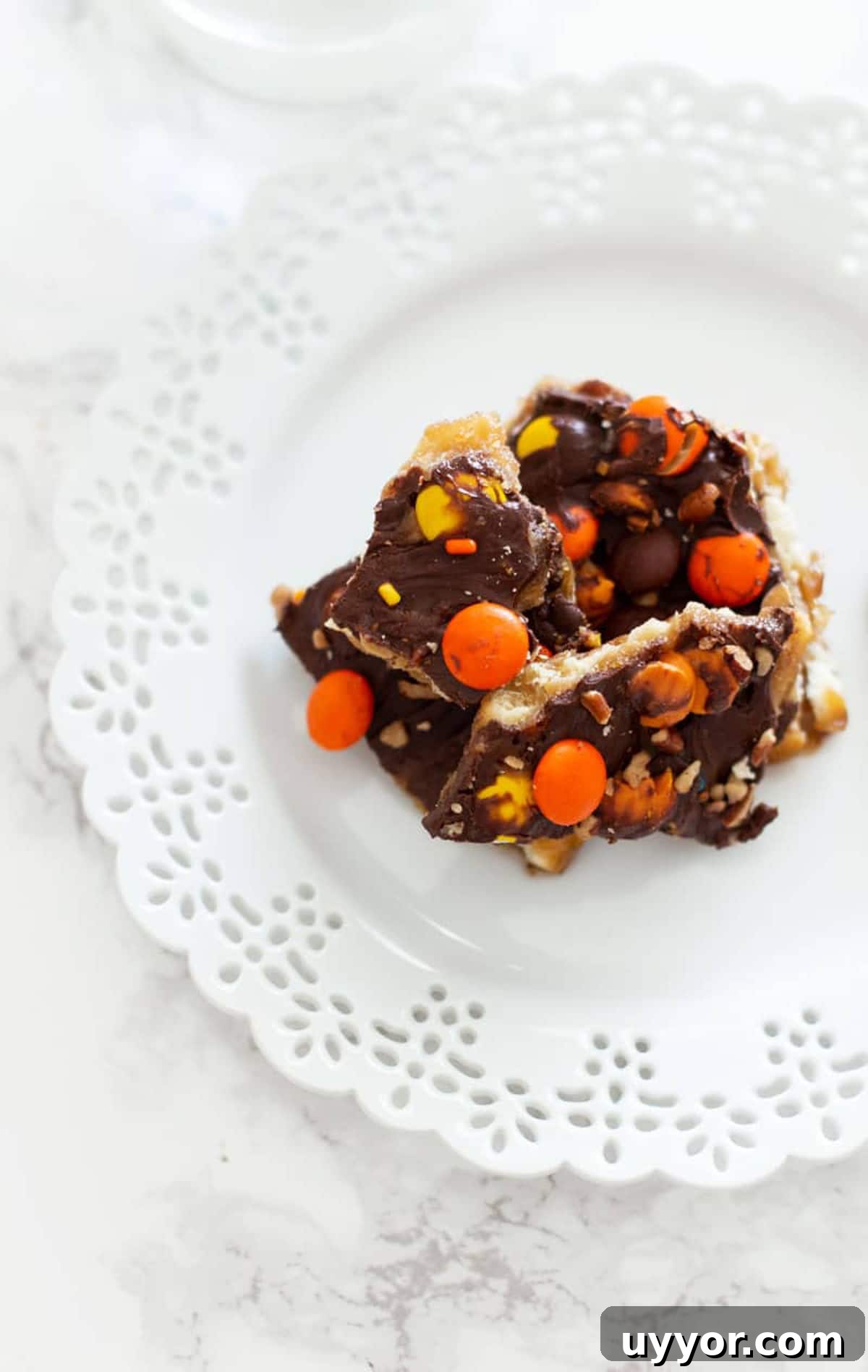Halloween Crack Candy Recipe: Sweet & Crunchy Toffee Treat 15 White late plate containing Halloween Candy Bark topped with chocolate, reese's pieces and pecans.