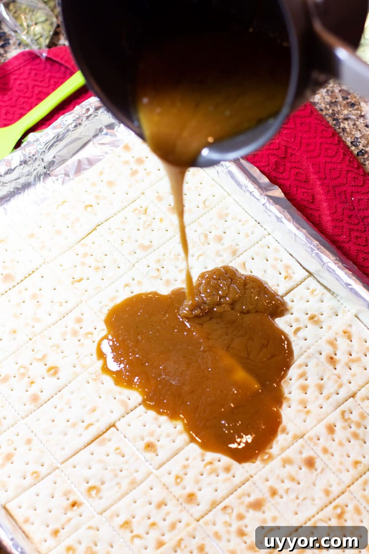 Halloween Crack Candy Recipe: Sweet & Crunchy Toffee Treat 9 Caramel sauce being poured onto a cookie sheet of saltine crackers.