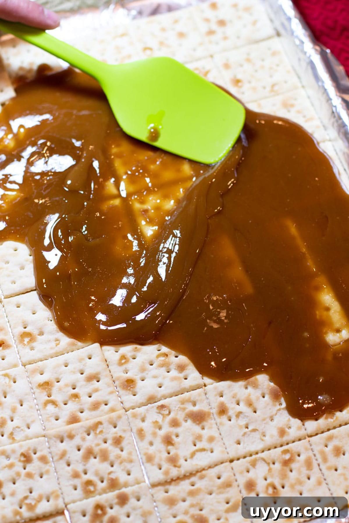 Halloween Crack Candy Recipe: Sweet & Crunchy Toffee Treat 10 Green spatula spreading homemade caramel onto saltine crackers.