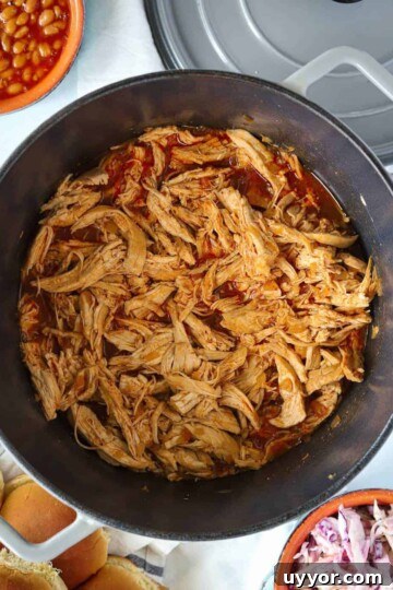 Dutch oven full of pulled chicken breast in bbq sauce with a side of slaw and beans.