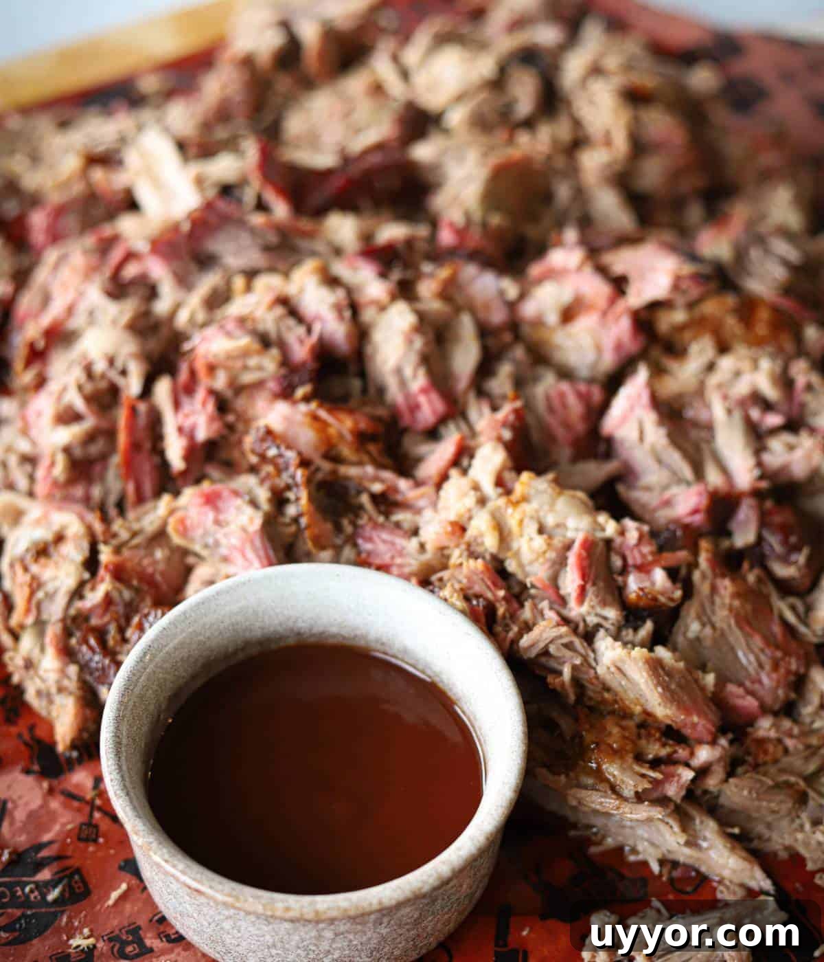 How to Smoke a Pork Butt for Tender, Flavorful Pulled Pork 4 Pulled pork shredded on a cutting board with a side of bbq sauce.