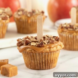 A caramel apple cupcake with caramel and pecan pieces on top and a popsicle stick in the center.