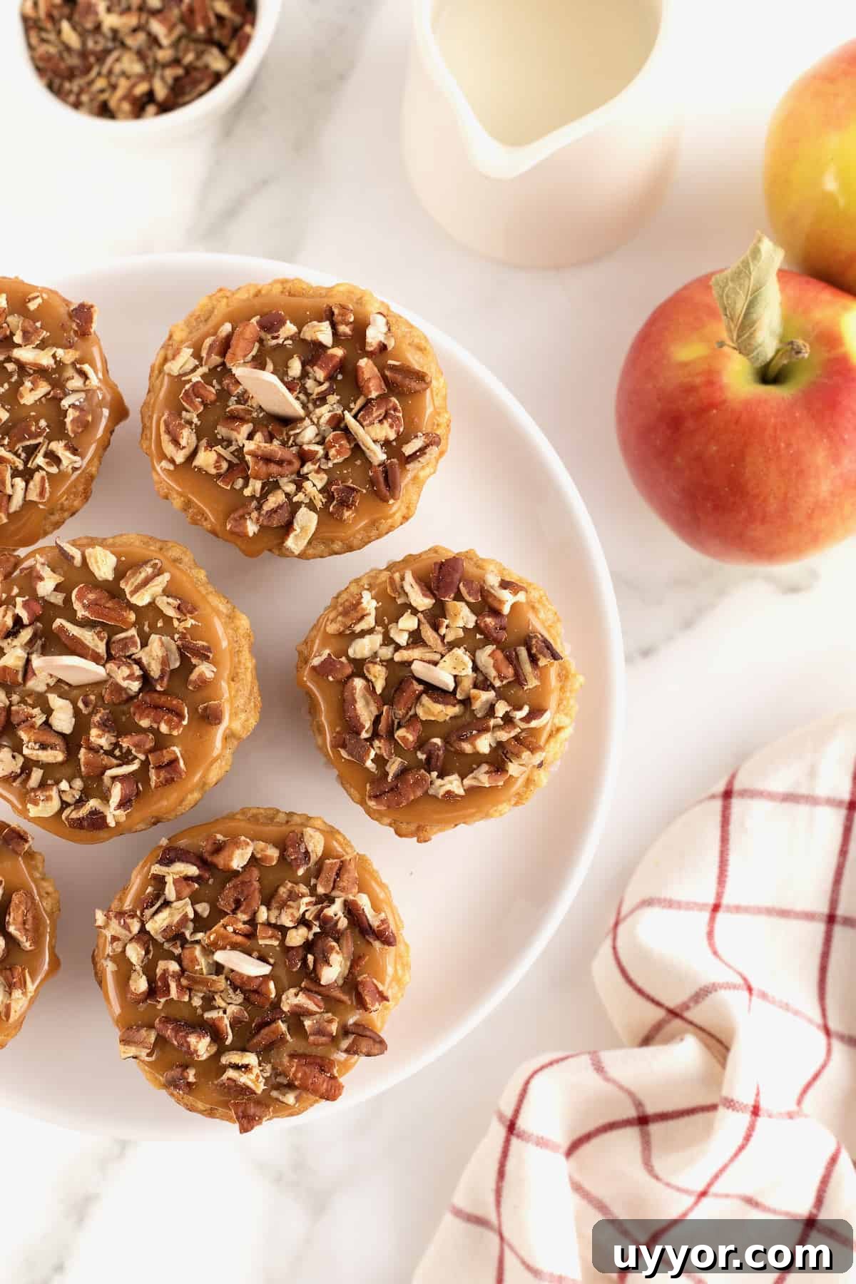 Caramel Apple Cupcake Recipe with Brown Butter Streusel 10 Caramel Apple Cupcakes on a white serving plate next to an apple and a tea towel.