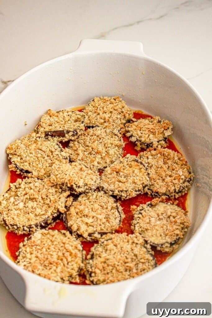 Classic Homemade Eggplant Parmesan Recipe for Crispy Layers 8 Breaded eggplant slices in a baking dish on top of sauce.